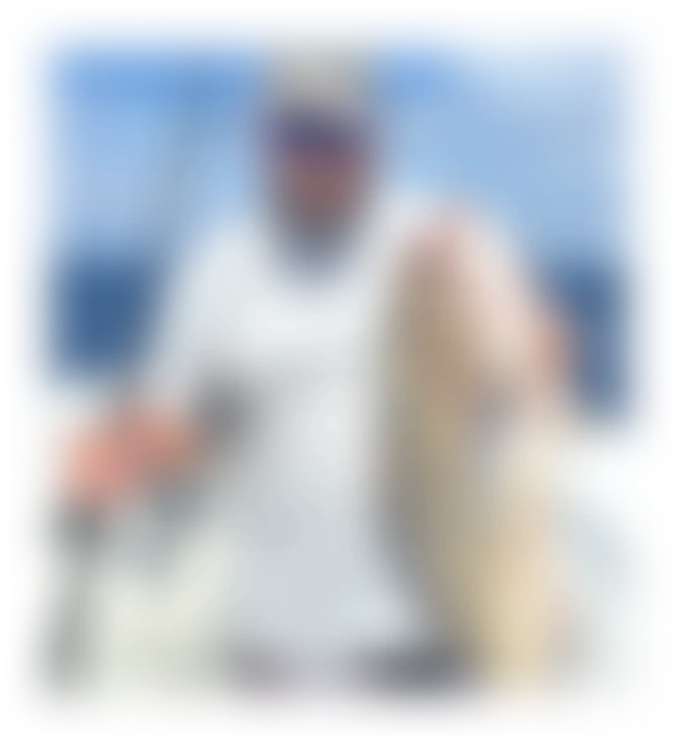 Man on a boat holding a fishing rod in one hand and a large caught fish in the other under a clear blue sky.