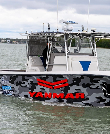 A gray camouflage boat equipped with a console and a YANMAR logo, gliding through calm waters under a cloudy sky.