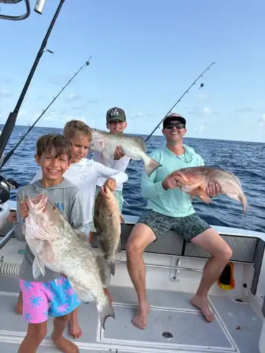 Four people on a boat hold large fish they caught, smiling proudly. The sea is calm, and fishing rods are visible, creating a joyful, adventurous mood.