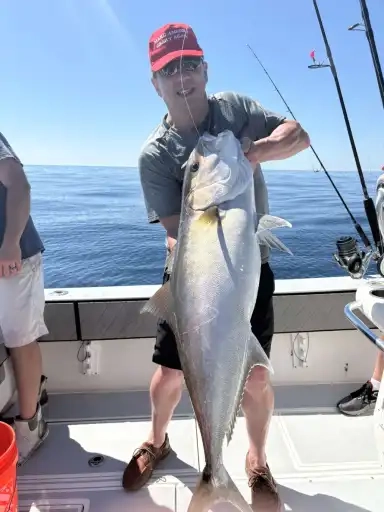 A person holding a large fish on a fishing boat, with calm ocean waters in the background.