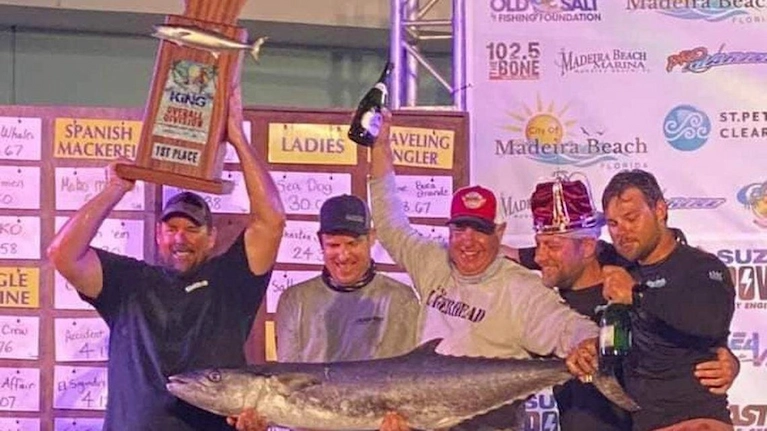 Group of men holding a large fish and a first-place trophy at a fishing tournament award ceremony.